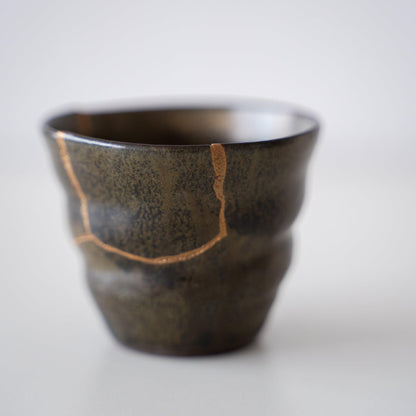 Close-up of a deep green sake cup repaired with Kintsugi, a traditional Japanese technique, showcasing the beautiful golden joinery.