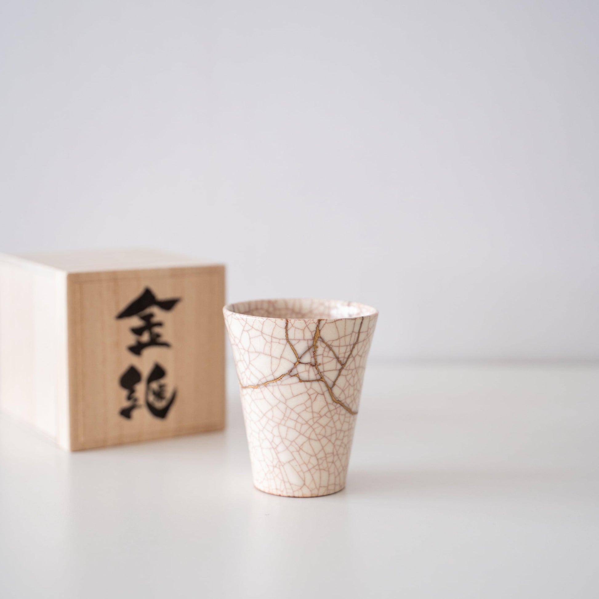 White cup repaired with Kintsugi, a traditional Japanese technique, presented in a paulownia wood box with the inscription "Kintsugi".
