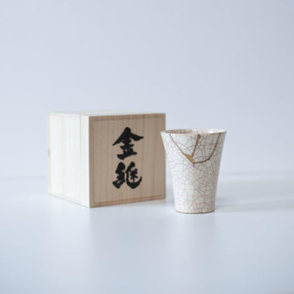 White cup repaired with Kintsugi, a traditional Japanese technique, presented in a paulownia wood box with the inscription "Kintsugi".