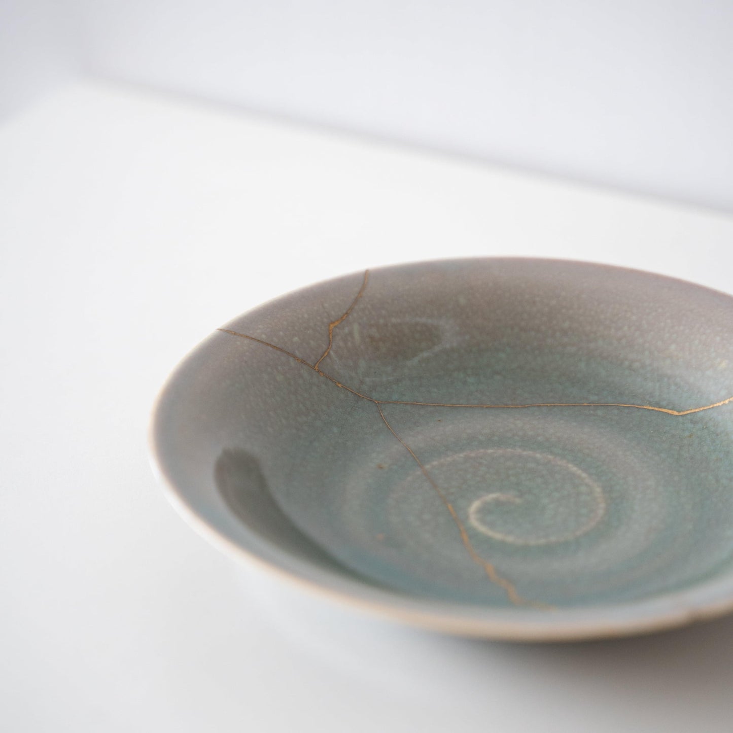 Pale green bowl repaired with Kintsugi, a traditional Japanese technique.