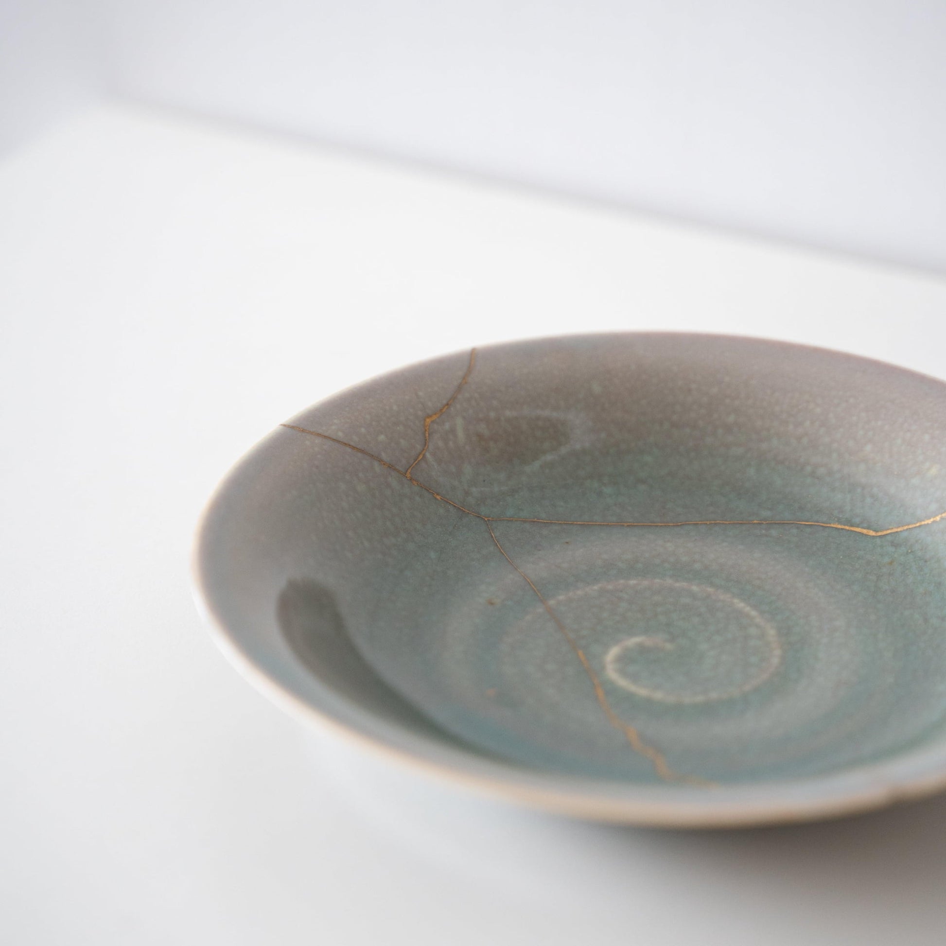 Pale green bowl repaired with Kintsugi, a traditional Japanese technique.
