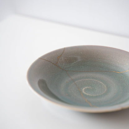 Pale green bowl repaired with Kintsugi, a traditional Japanese technique.