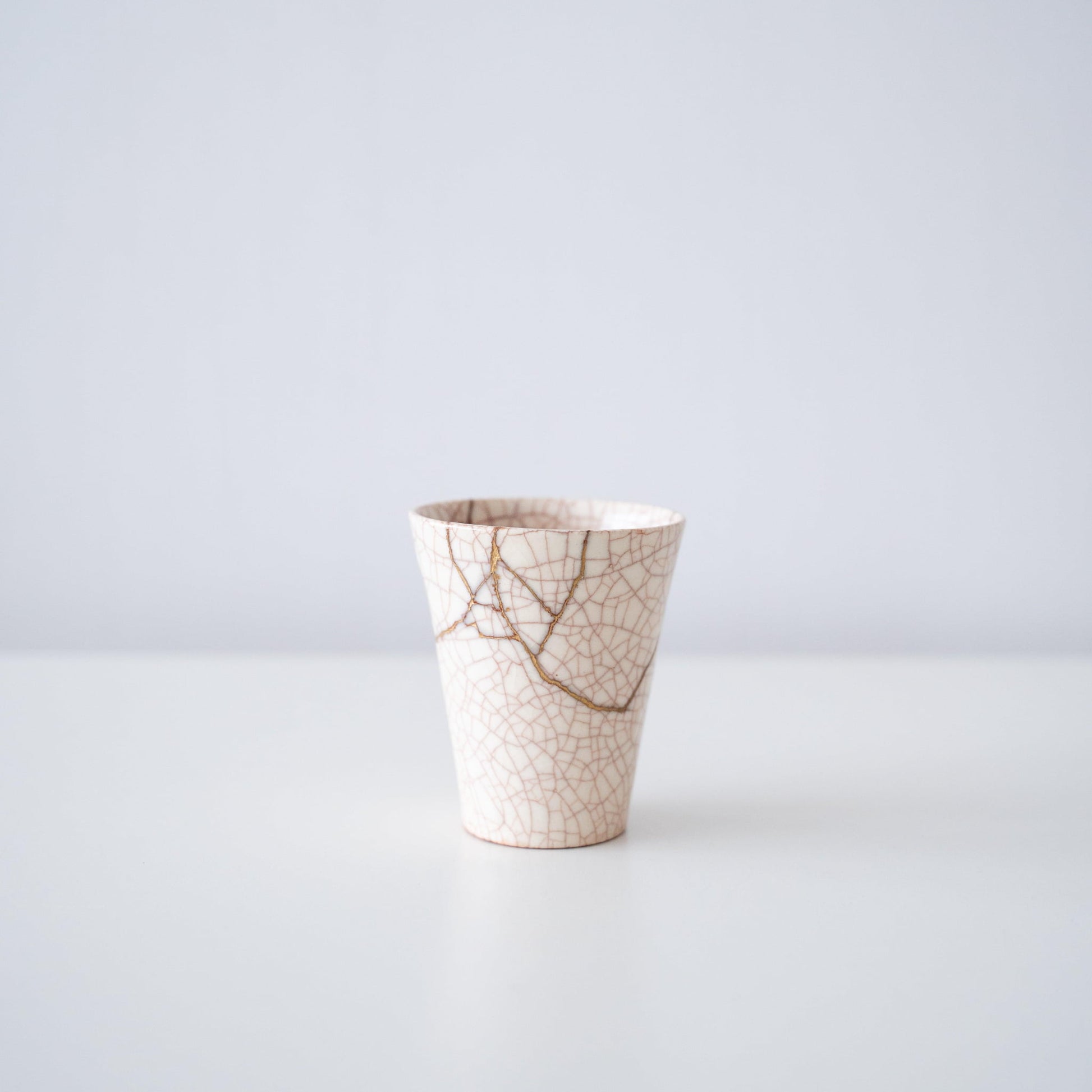 White cup repaired with Kintsugi, a traditional Japanese technique, showcasing the beautiful golden joinery.