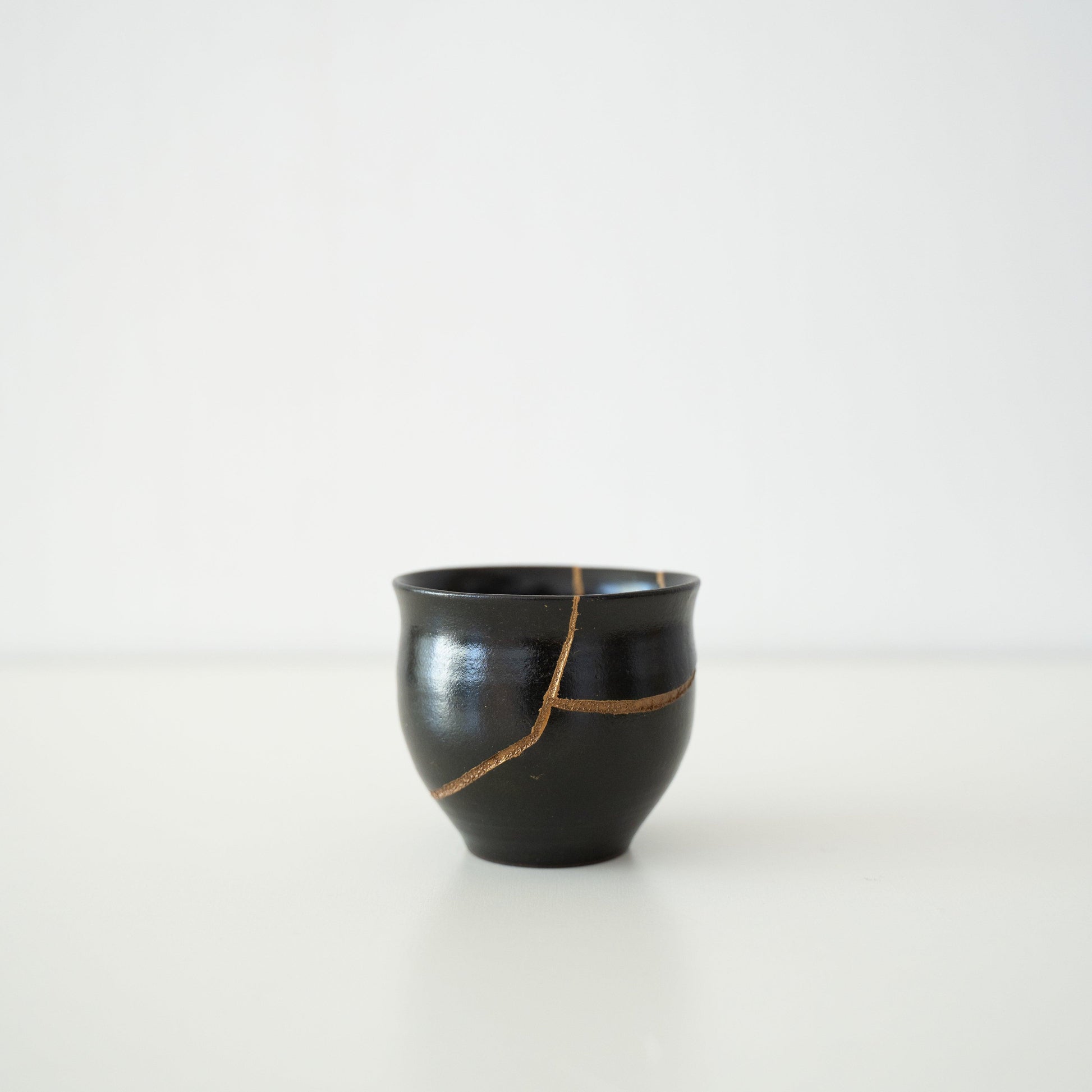 Japanese sake cup named "Shikkoku Rai" (Jet-Black Thunder), repaired with gold lacquer using the traditional Kintsugi technique.