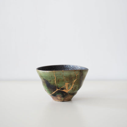 Deep green tea bowl repaired with Kintsugi, a traditional Japanese technique, showcasing the beauty of imperfection.