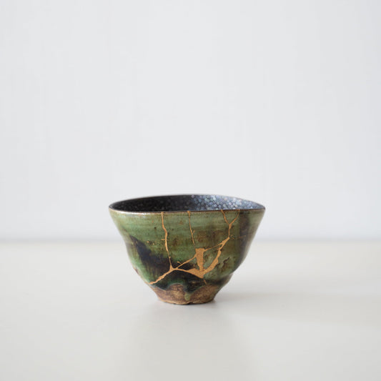 Deep green tea bowl repaired with Kintsugi, a traditional Japanese technique, showcasing the beauty of imperfection.