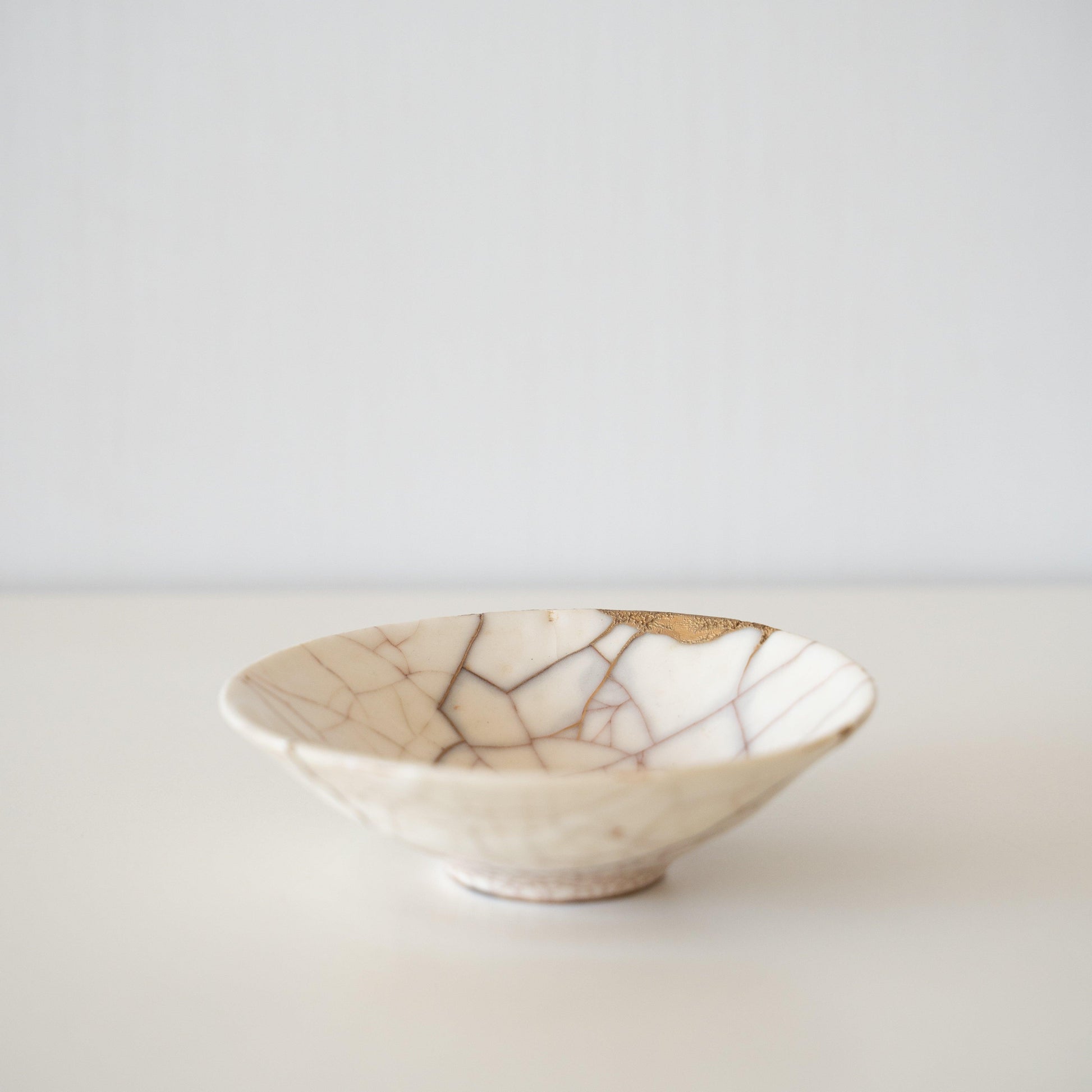 White ceramic bowl repaired with kintsugi, a traditional Japanese art of mending broken pottery with gold lacquer, showcasing the beauty of imperfection and embracing the concept of wabi-sabi.