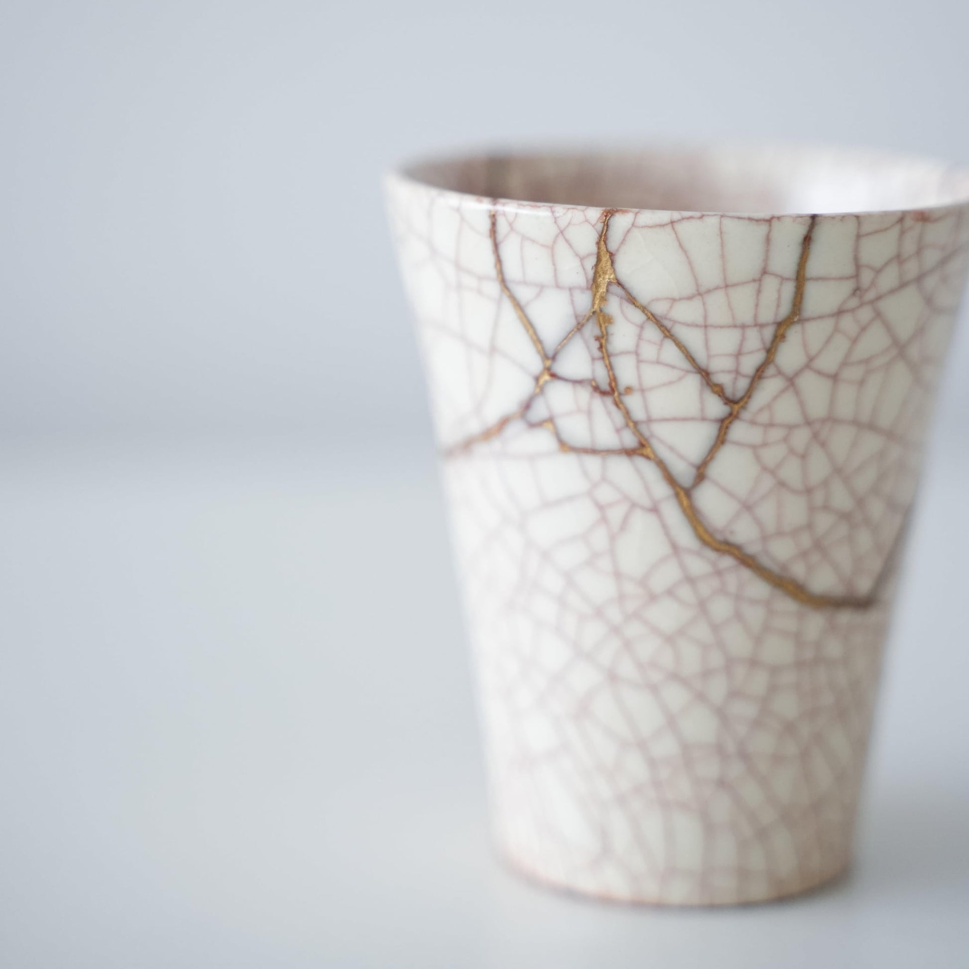 White cup repaired with Kintsugi, a traditional Japanese technique, showcasing the beautiful golden joinery.