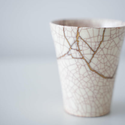 White cup repaired with Kintsugi, a traditional Japanese technique, showcasing the beautiful golden joinery.
