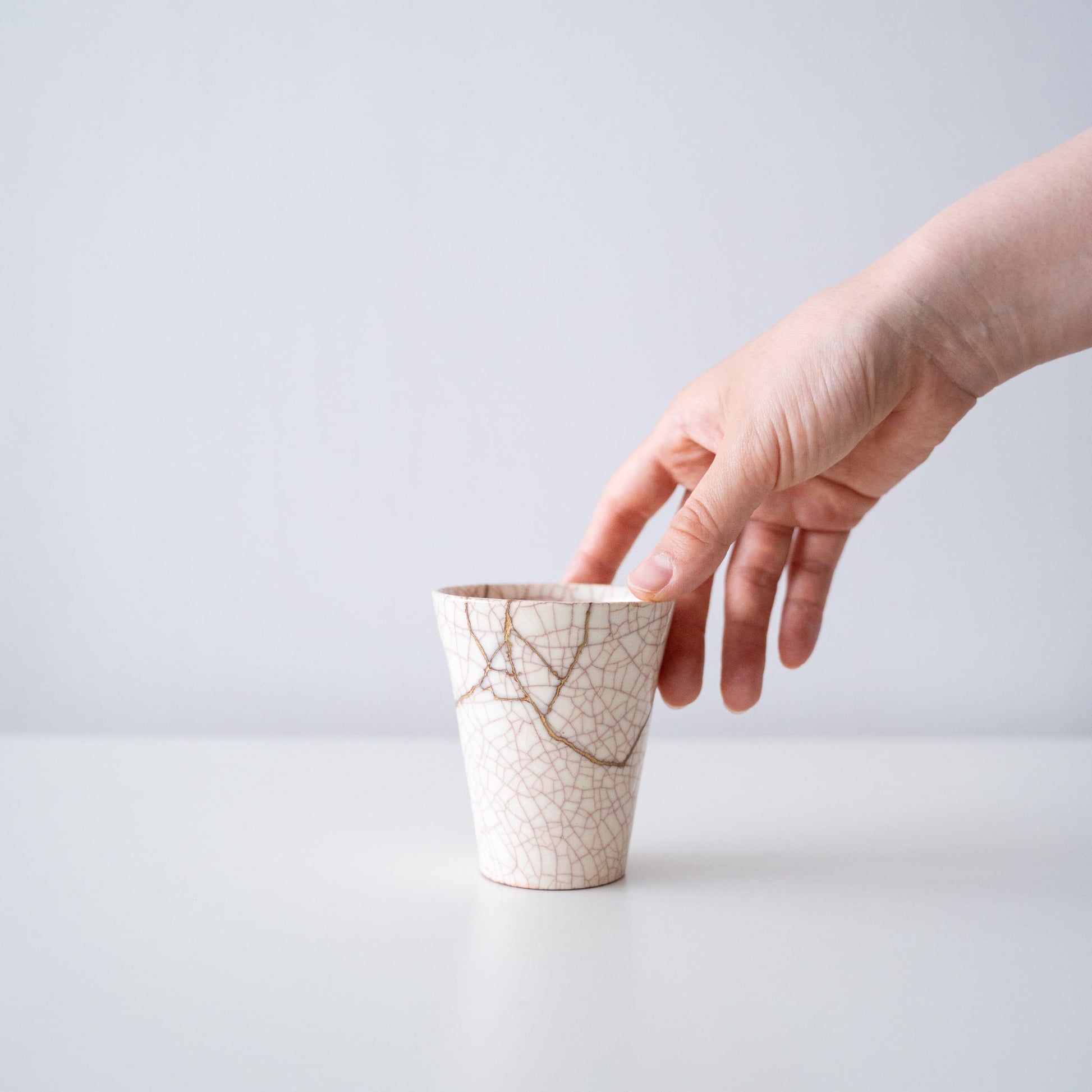 Hand holding a white cup repaired with Kintsugi, a traditional Japanese technique.