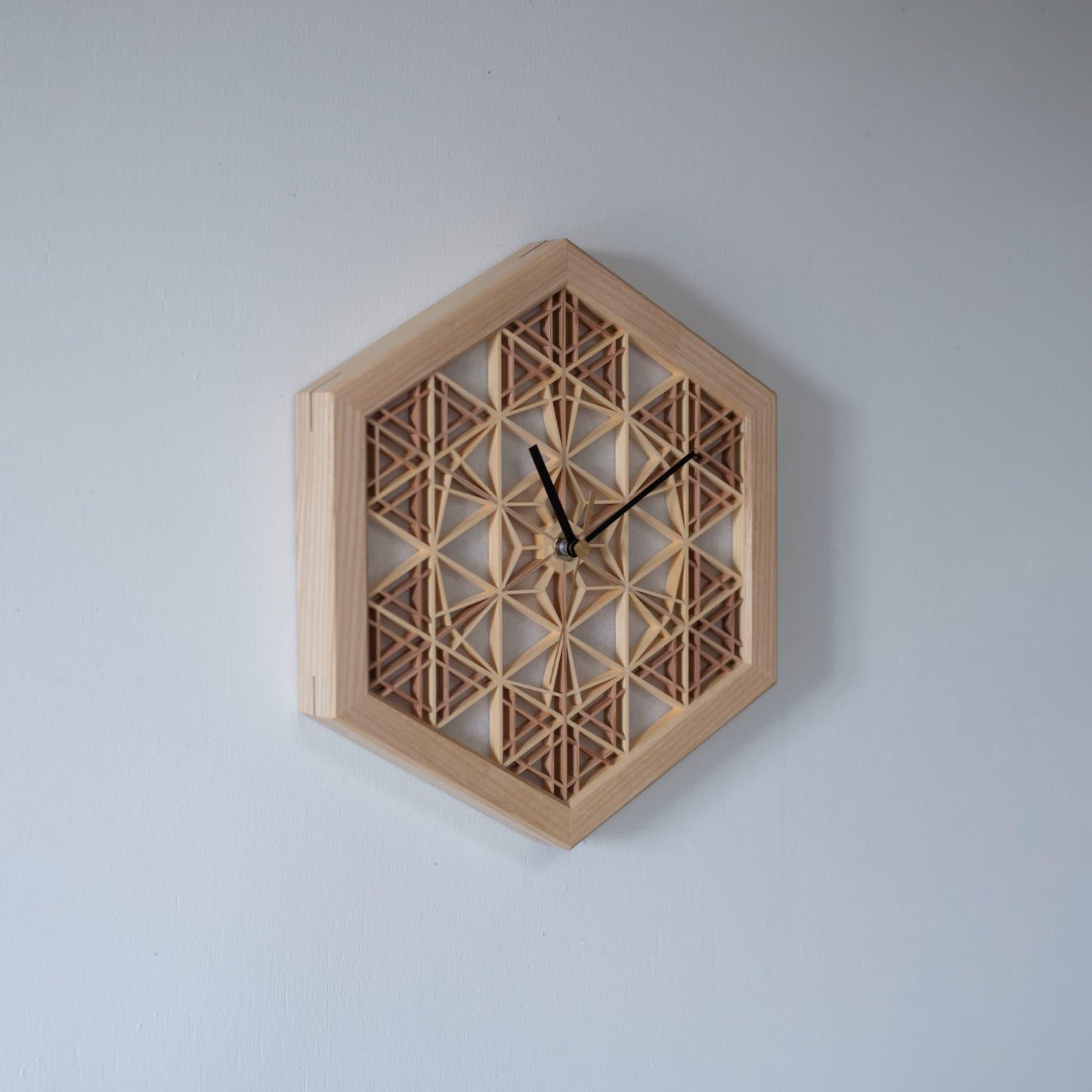 A kumiko clock hanging on a wall, viewed from the left side. The intricate wooden latticework is a testament to traditional Japanese craftsmanship.