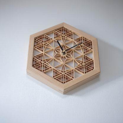 A kumiko clock hanging on a wall, viewed from below. The intricate wooden latticework creates a stunning visual effect.