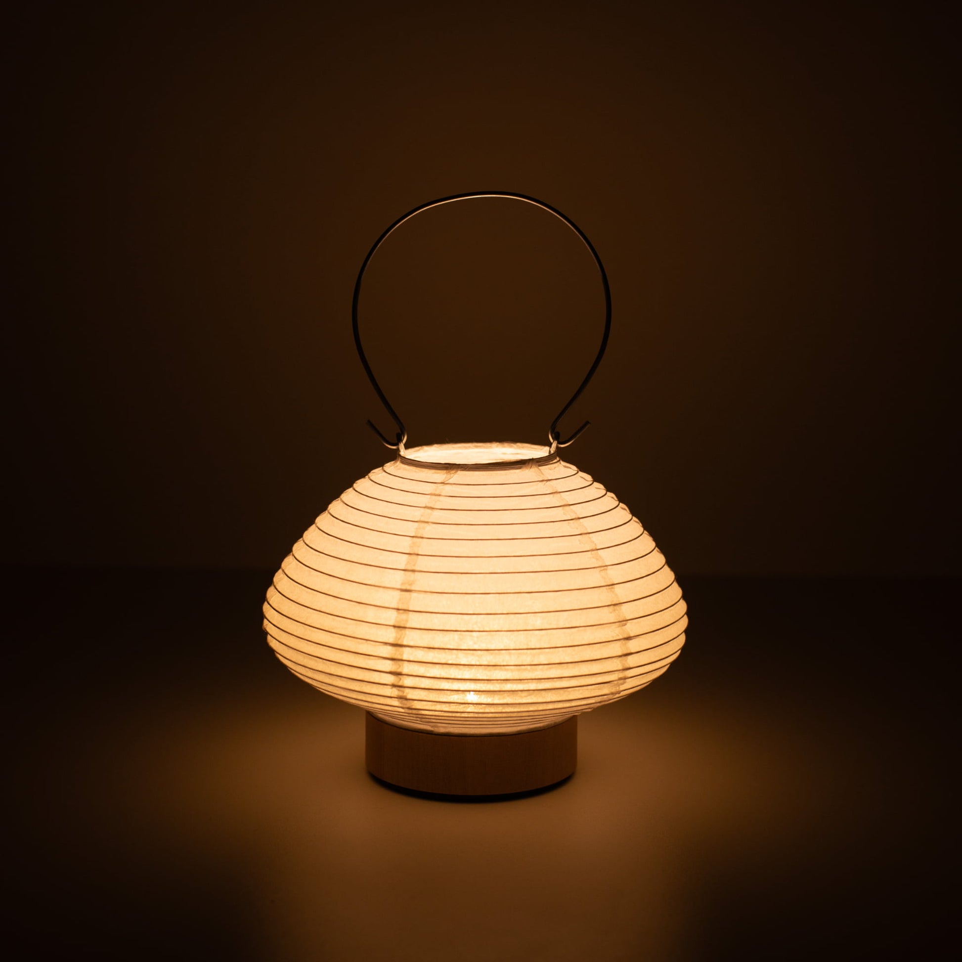 Hand holding a portable paper table lamp resembling a traditional Japanese lantern, crafted with Gifu lantern techniques and Mino washi paper.