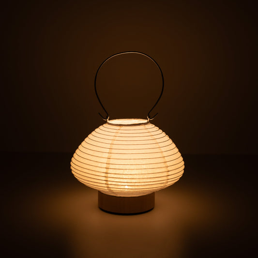 Hand holding a portable paper table lamp resembling a traditional Japanese lantern, crafted with Gifu lantern techniques and Mino washi paper.
