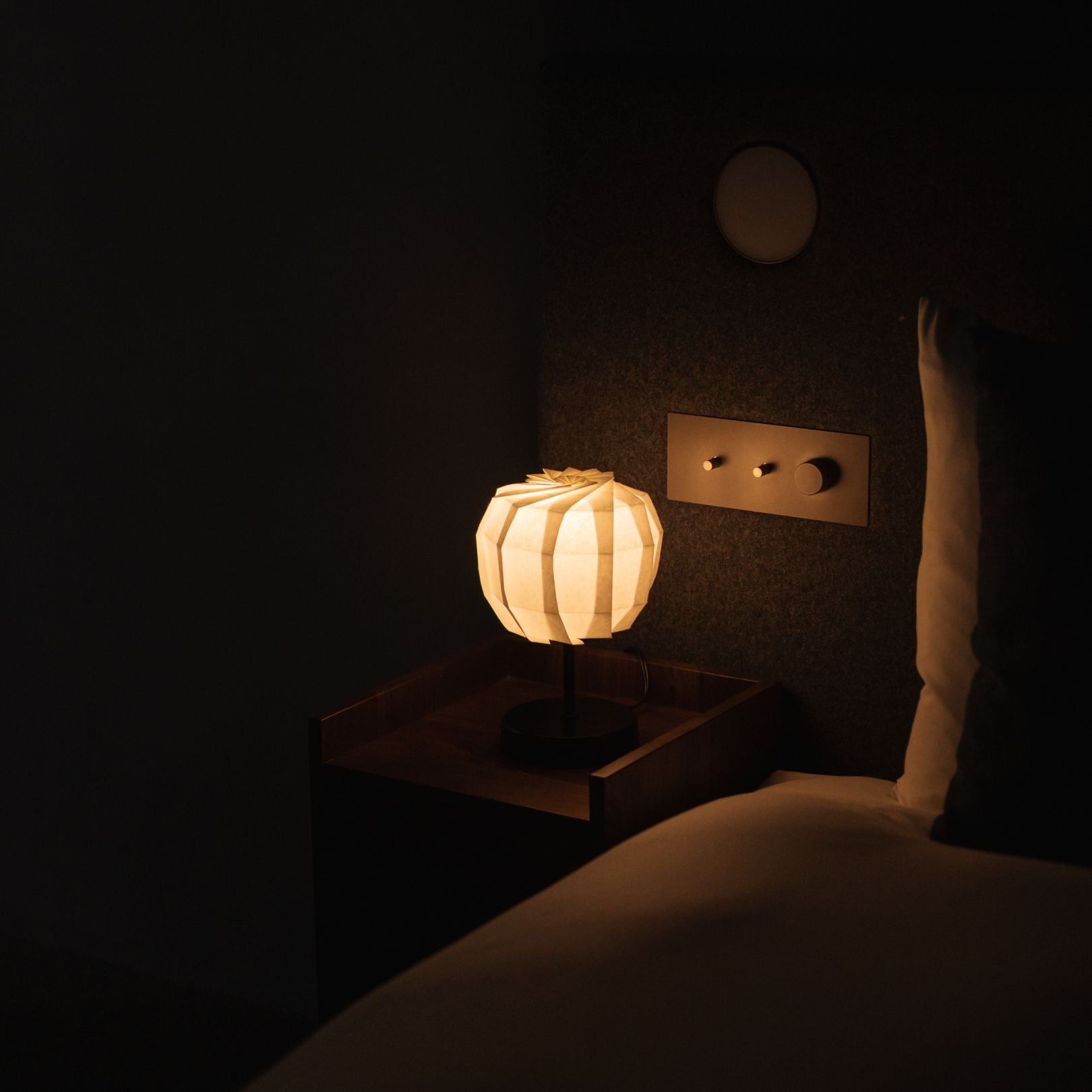 Japanese Paper Table Lamp "Flower of Light maru with Stand" lit on a wooden bedside table