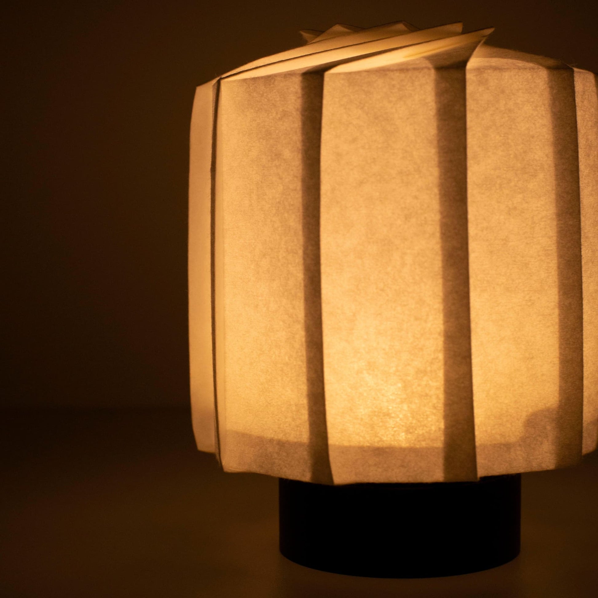 Hand holding a frameless Japanese table lamp crafted with traditional Kyo-hyogu and origami techniques, featuring a unique illuminated origami pattern.