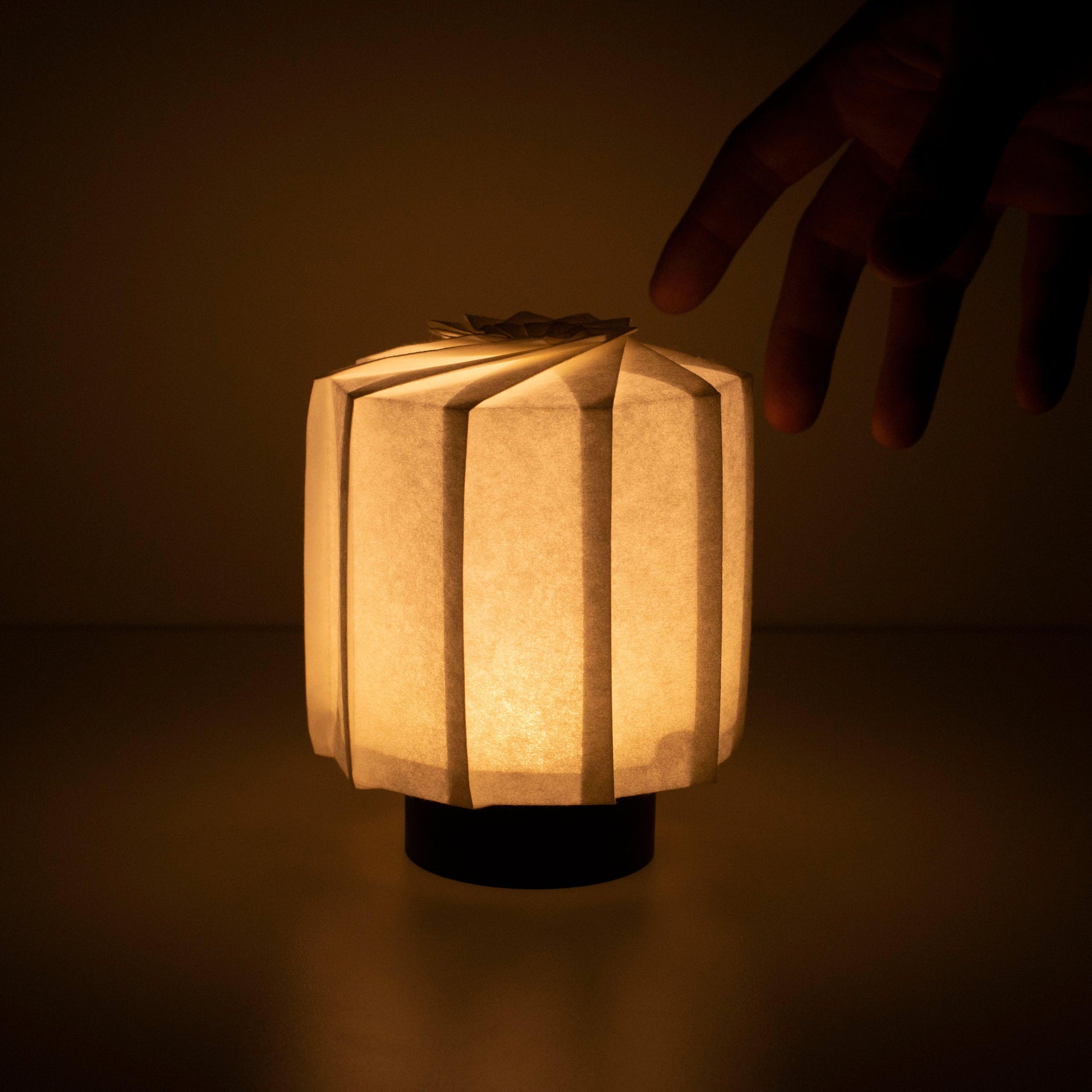 Hand holding a frameless Japanese table lamp crafted with traditional Kyo-hyogu and origami techniques, featuring a unique illuminated origami pattern.with hand