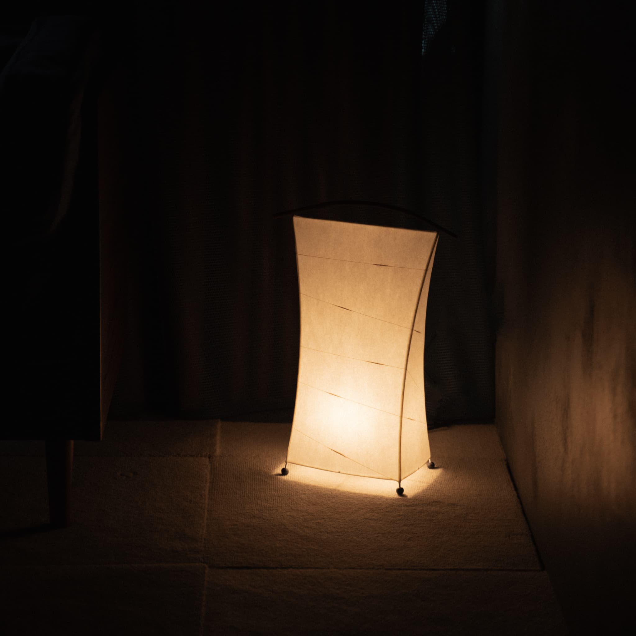 Japanese Paper Floor Lamp "NOW" emitting warm light in a dimly lit room