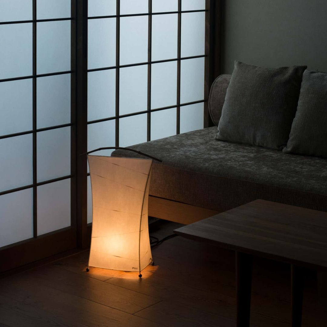 Japanese floor lamp emitting "NOW" a warm glow in the corner of a dimly lit Japanese-style living room