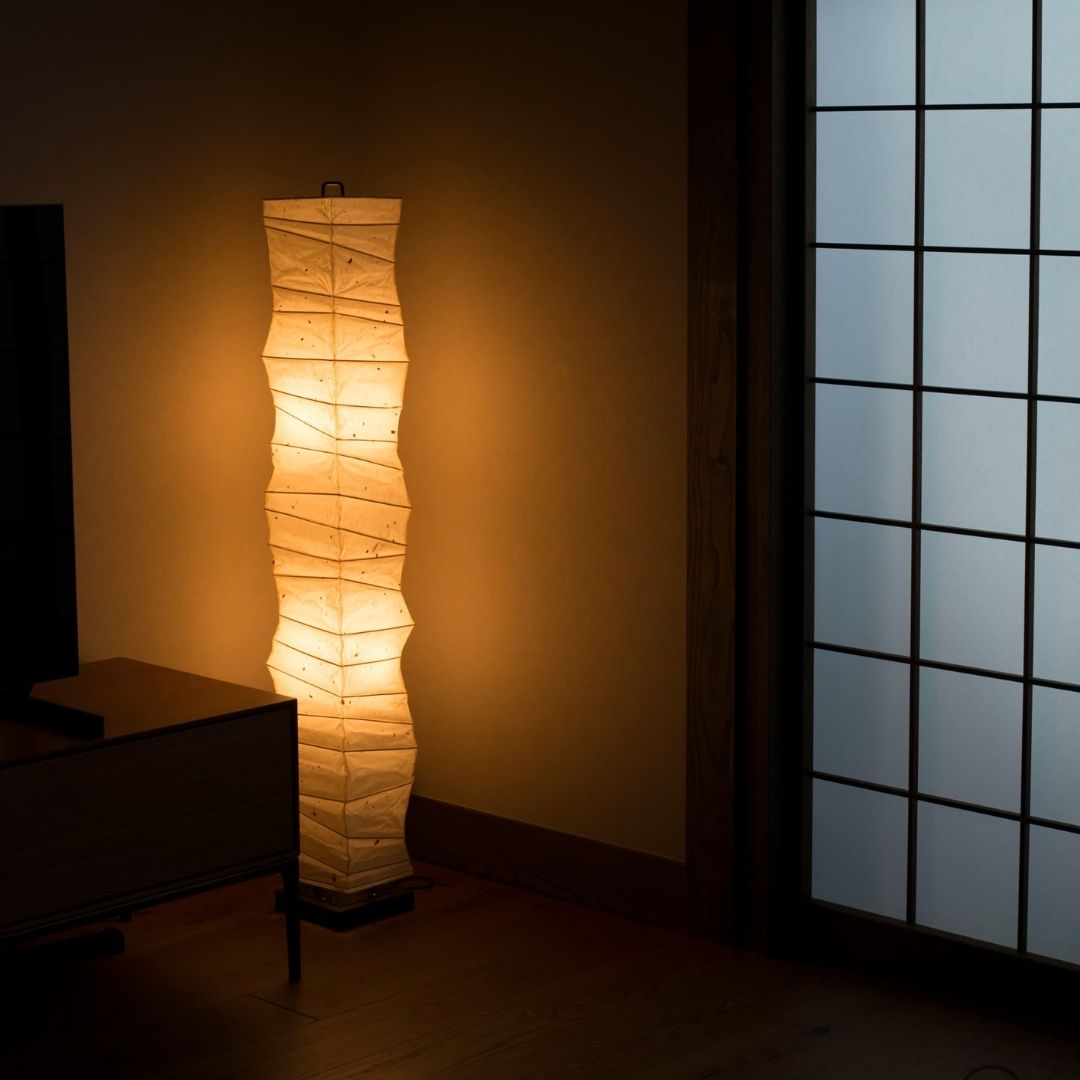 Japanese floor lamp "SLENDER" emitting a warm glow in the corner of a dimly lit Japanese-style living room