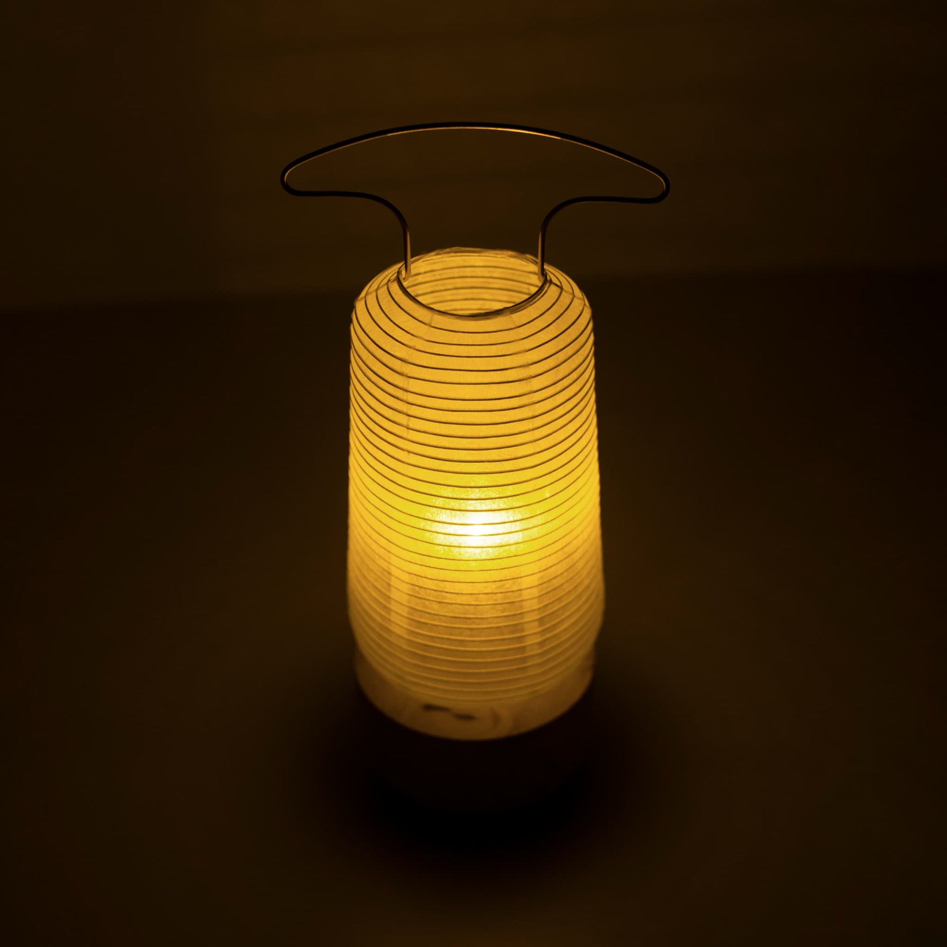 A traditional Japanese paper lantern emitting warm light in a dim room