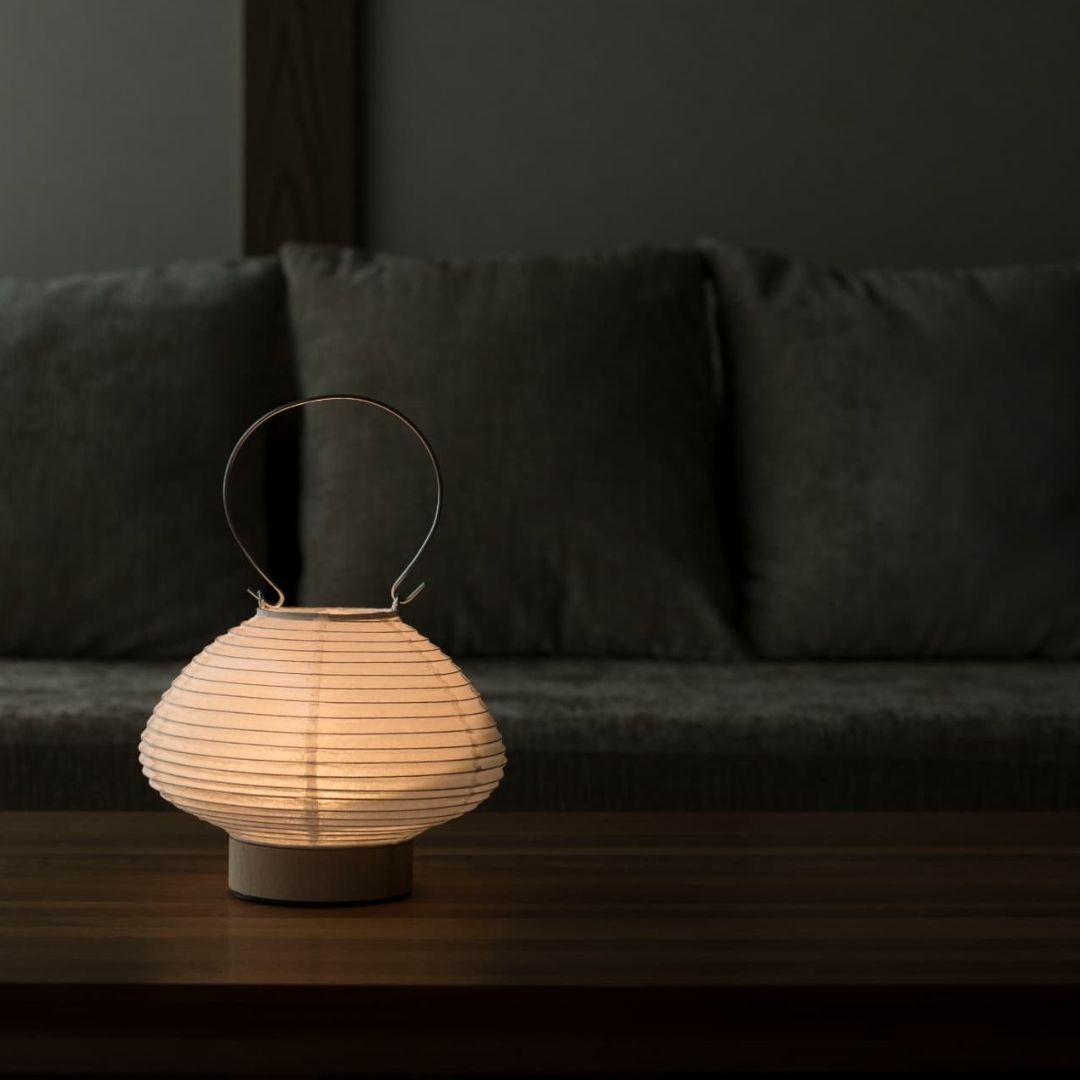 Japanese paper table lamp shaped like a lantern emitting a warm glow on a wooden table in a living room