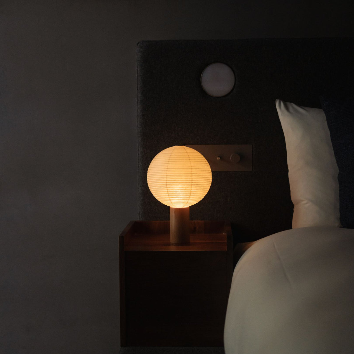 Japanese Paper Table Lamp "TORCHIN CIRCLE" emitting warm light on a bedside table in a Japandi bedroom