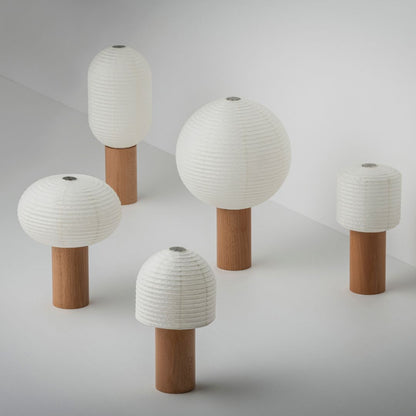 Five portable lamps, "TORCHIN", with beautiful white washi paper and brown wooden handles, randomly arranged in a bright white room. The lampshades are made of Japanese washi paper from Yame-chochin lanterns, and each lamp has a wooden cylindrical handle.