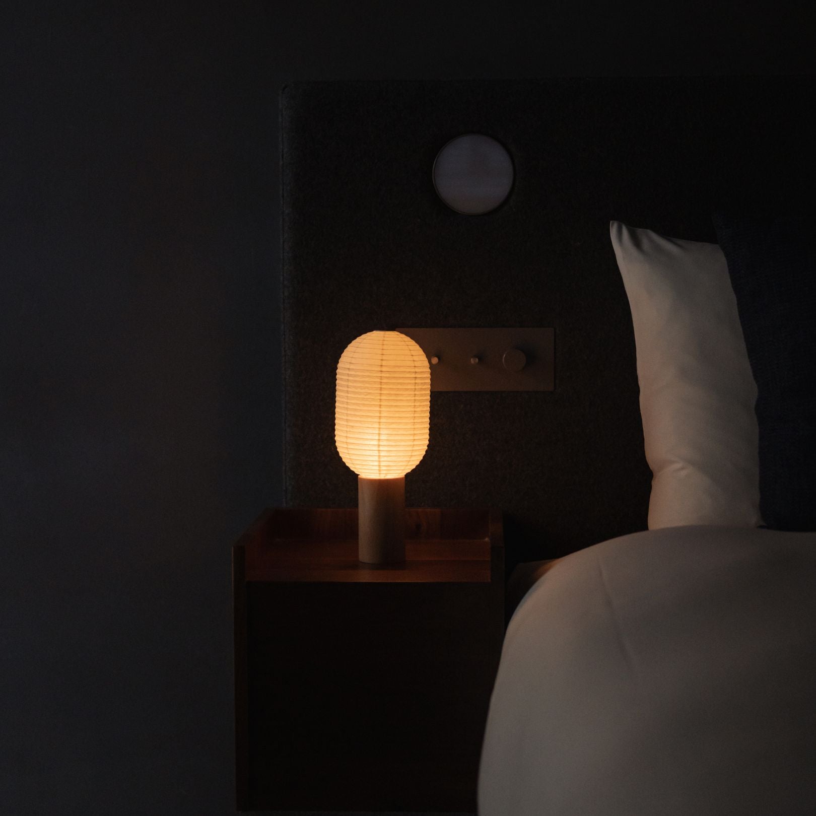 Japanese Paper Table Lamp "TORCHIN VERTICAL" emitting warm light on a bedside table in a Japandi bedroom