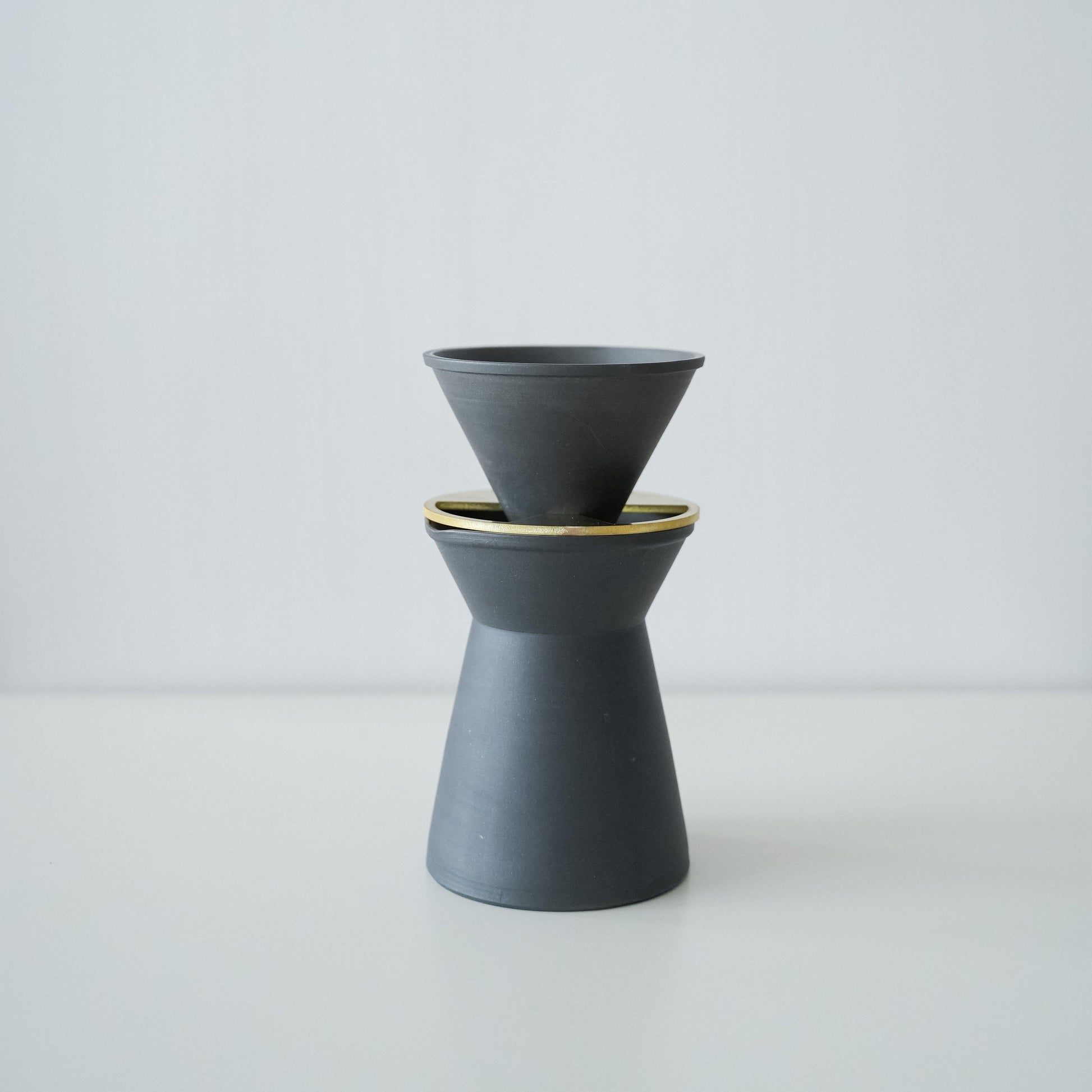 A set of minimalist black and white Banko ware coffee server and dripper on a wooden kitchen table.