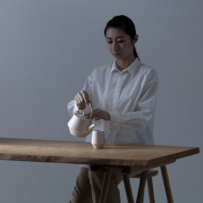 Woman serving Japanese green tea with teapot and yunomi tea cup on wooden table