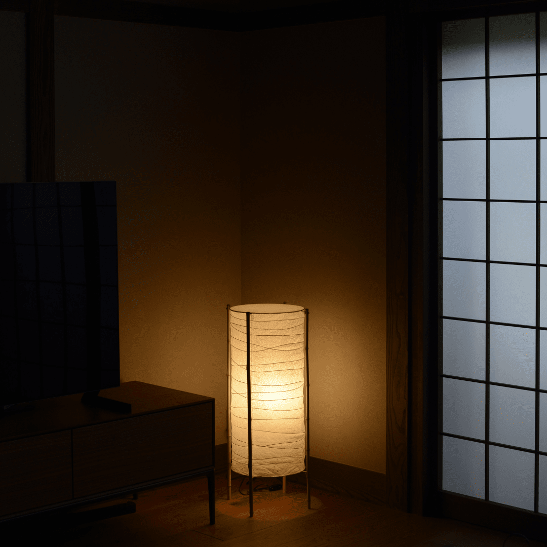 Japanese washi paper lamp with bamboo frame, placed in a traditional room, emitting warm light.