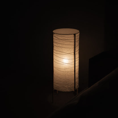 Dimly lit room with a Japanese cylindrical washi paper lamp and bamboo frame, casting a warm glow