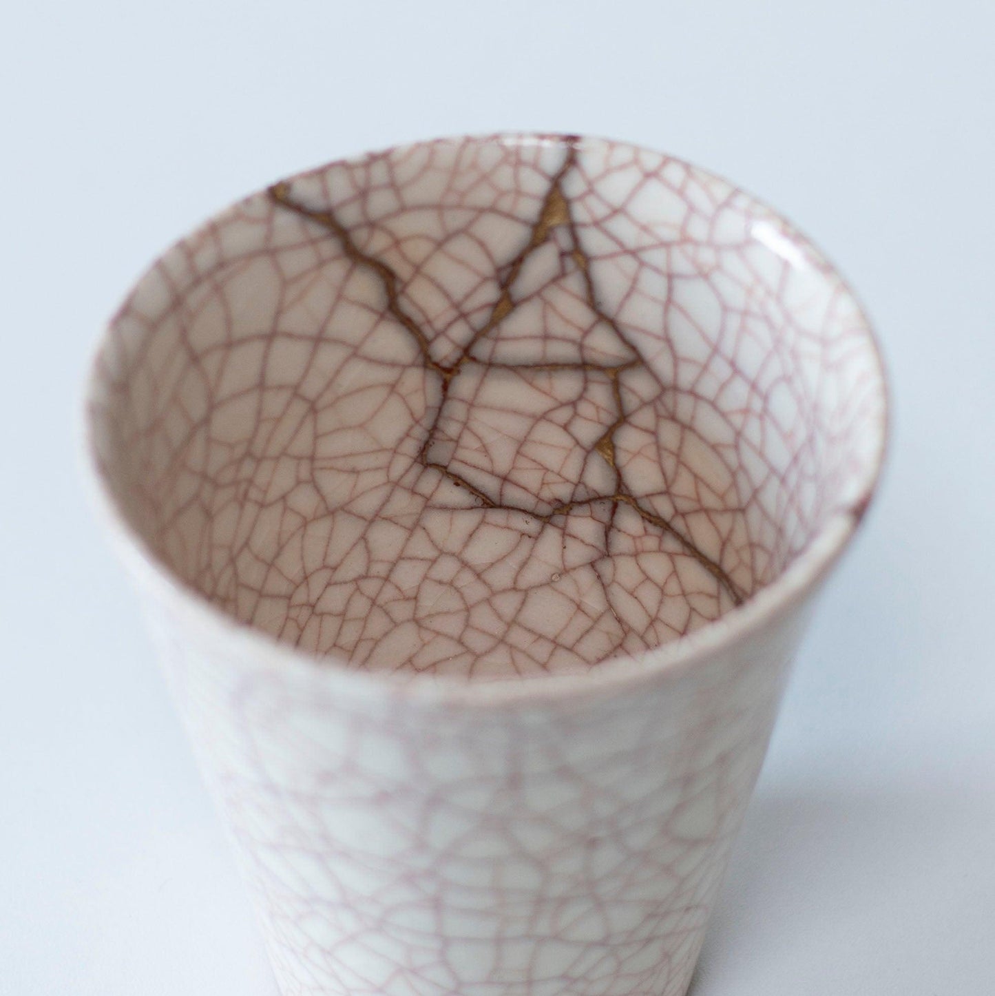 White cup repaired with Kintsugi, a traditional Japanese technique, presented in a paulownia wood box with the inscription "Kintsugi".