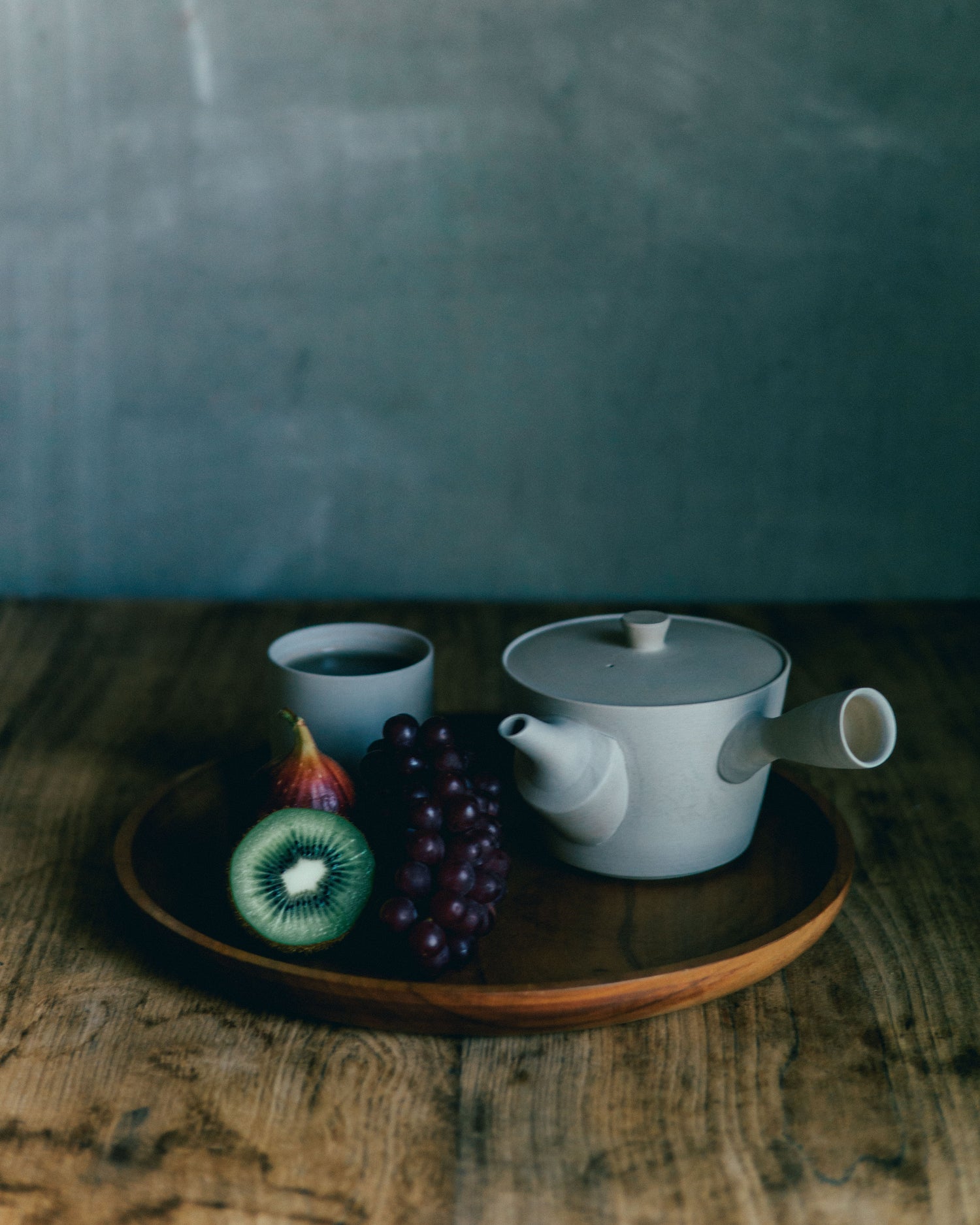 A white traditional Banko ware teapot and fruits on a tray.