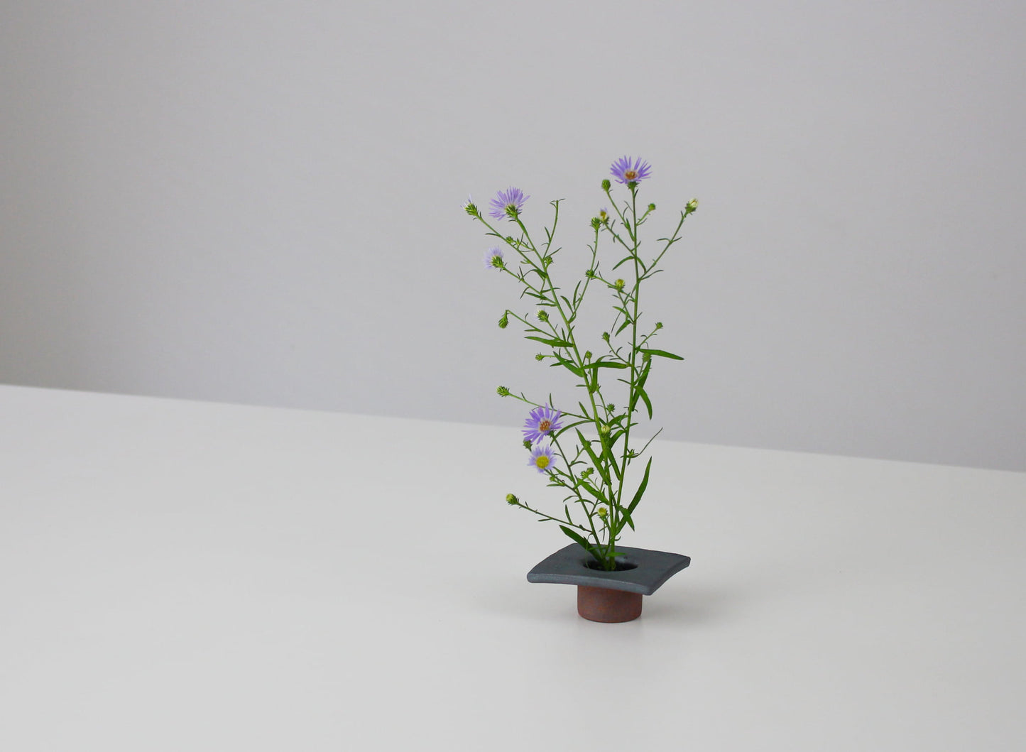 A Japanese iron-colored ikebana vase on a white table. 