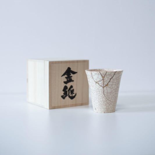 White cup repaired with Kintsugi, a traditional Japanese technique, presented in a paulownia wood box with the inscription "Kintsugi".