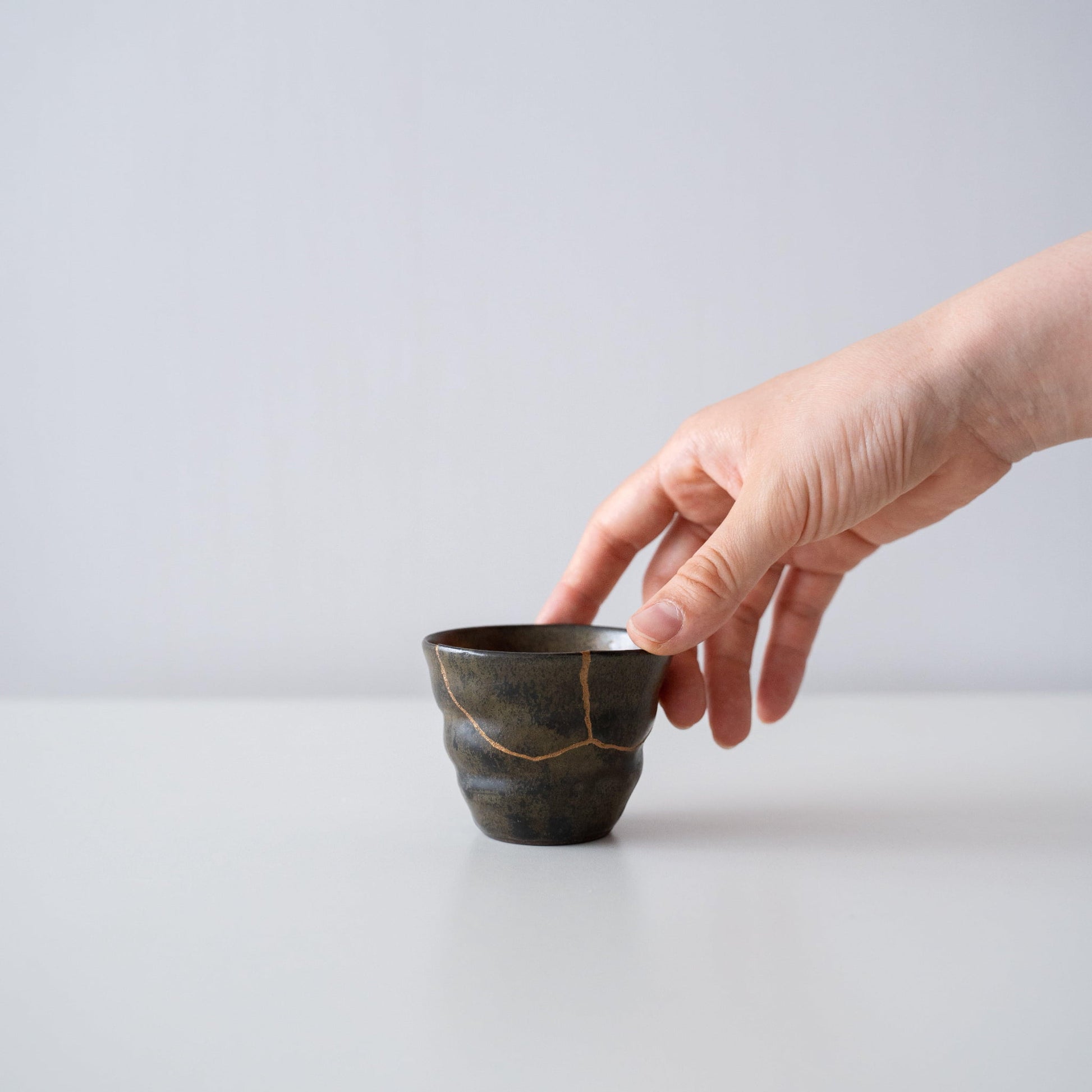 Hand holding Kintsugi Sake Cup "Thunder Moss", showing its size and how it fits in the hand