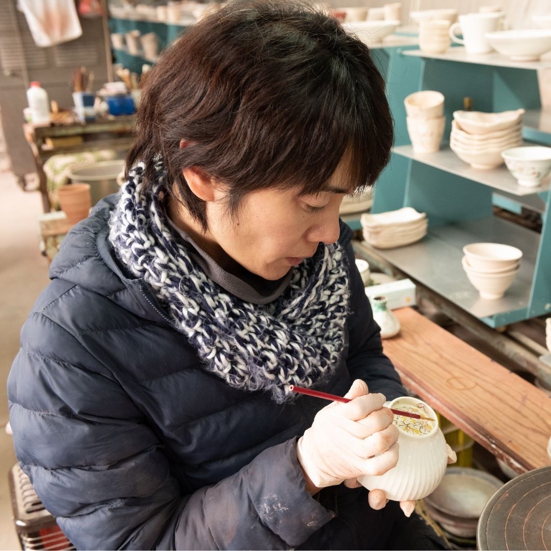 A Buzan Kiln artisan hand-painting a Japanese Mino Ware matcha bowl in her pottery studio, showing delicate brushwork and traditional craftsmanship.