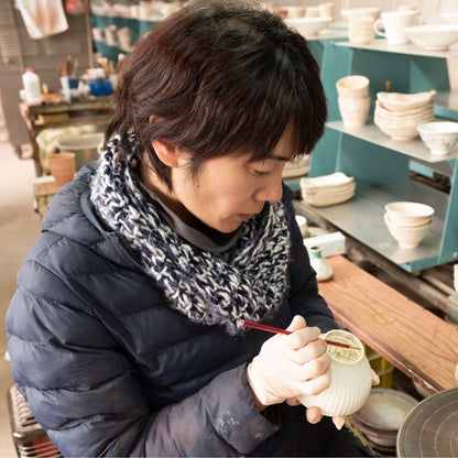 A Buzan Kiln artisan hand-painting a Japanese Mino Ware matcha bowl in her pottery studio, showing delicate brushwork and traditional craftsmanship.