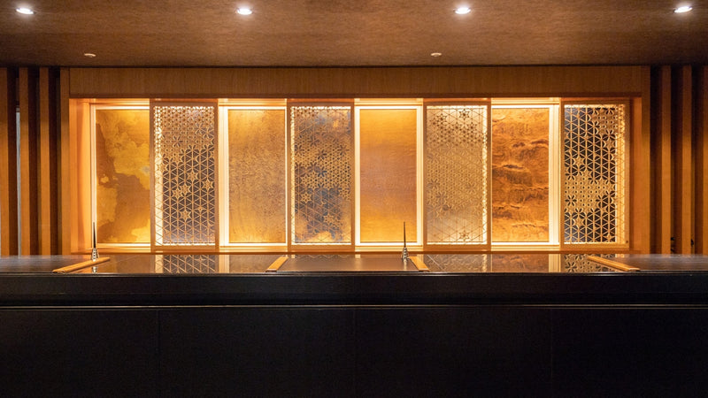 An elegant hotel reception area featuring a large-scale Japanese Kumiko-zaiku woodwork panel as a backdrop for the front desk.