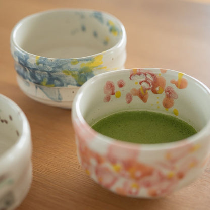 Angled view of the Shino ware matcha bowl collection on a wooden table, featuring the "Flower" bowl with prepared green matcha tea and the other two designs.