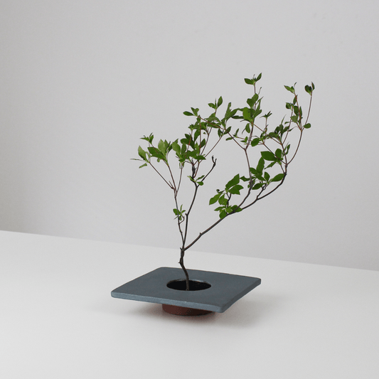 A minimalist iron ikebana vase inspired by traditional Japanese roof tiles, featuring a kenzan (flower frog) for arranging flowers.