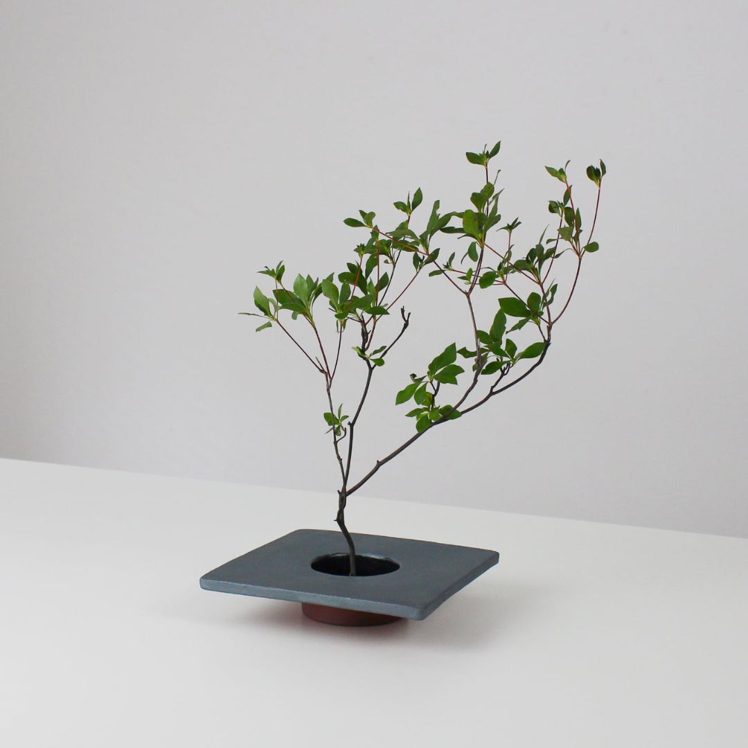 A minimalist iron ikebana vase inspired by traditional Japanese roof tiles, featuring a kenzan (flower frog) for arranging flowers.