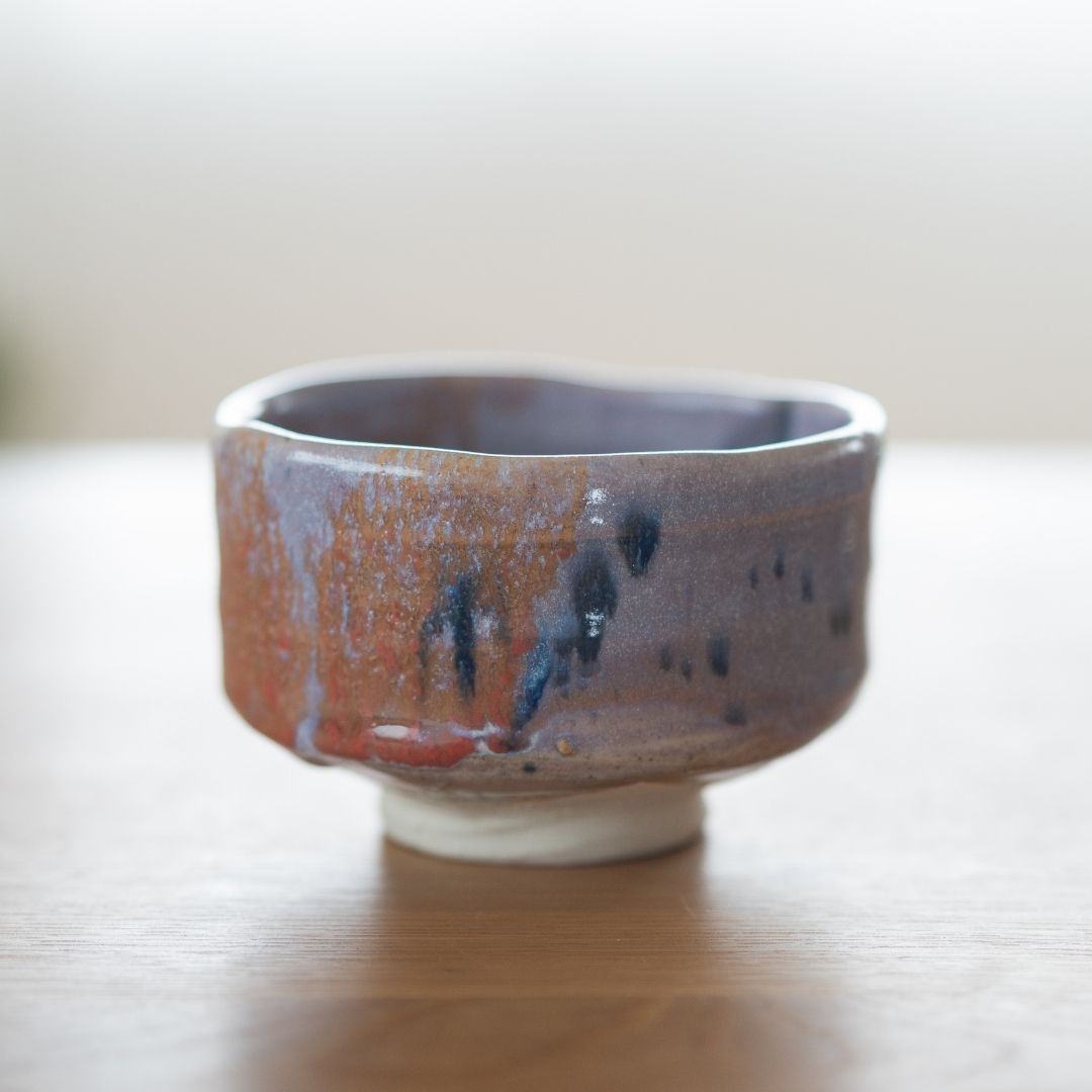 Front-facing shot of the handcrafted Mino Ware matcha bowl, featuring the thick, spontaneous Navy and Red Splash glaze and the unique Kinyo glaze undertones, displayed on a natural wood surface.