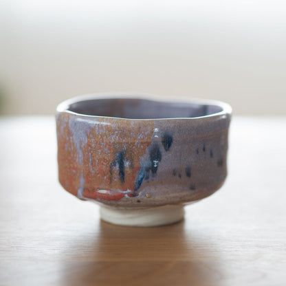 Front-facing shot of the handcrafted Mino Ware matcha bowl, featuring the thick, spontaneous Navy and Red Splash glaze and the unique Kinyo glaze undertones, displayed on a natural wood surface.