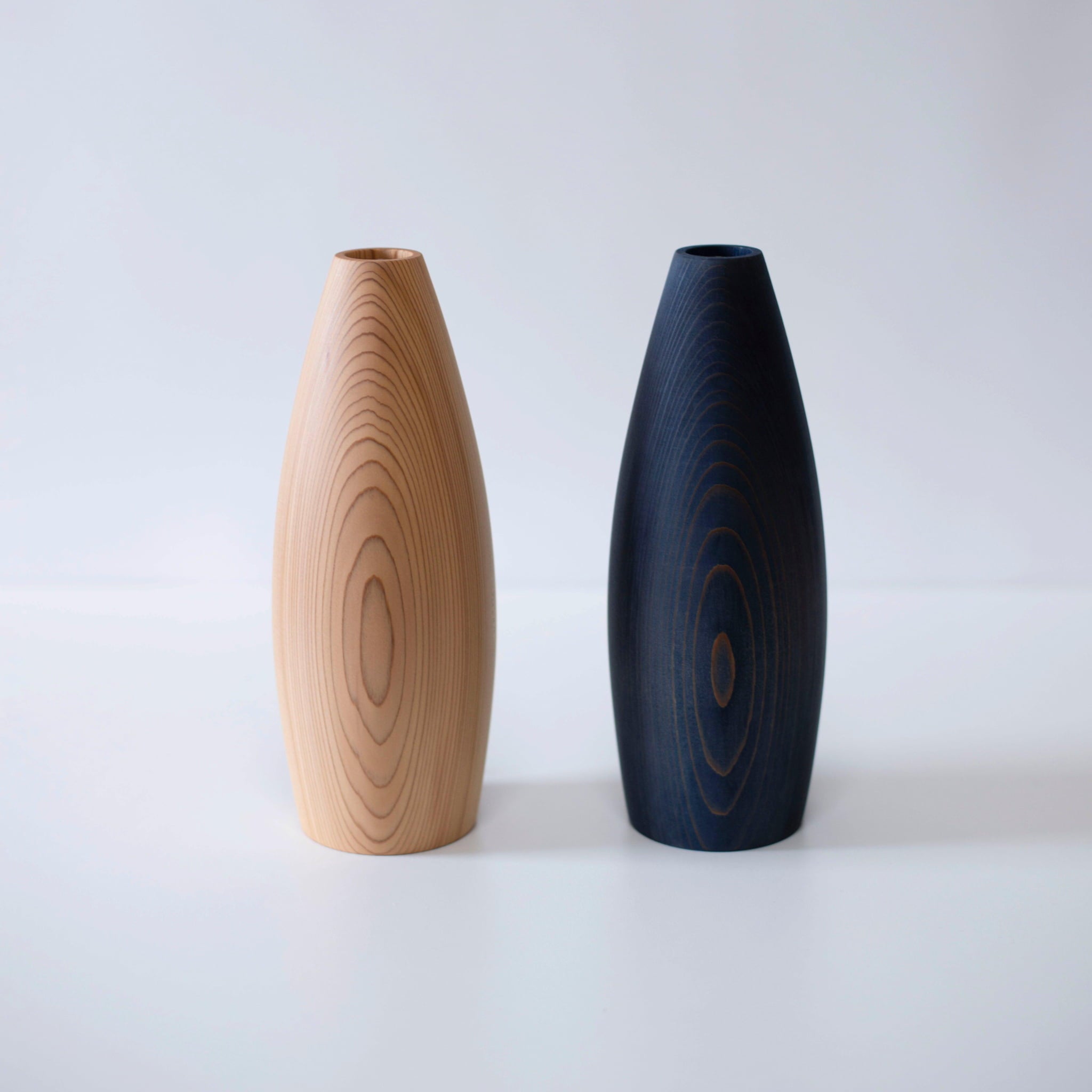 A pair of vases made from natural cedar wood, showcasing the beauty of the wood's grain and the deep blue of indigo dye.