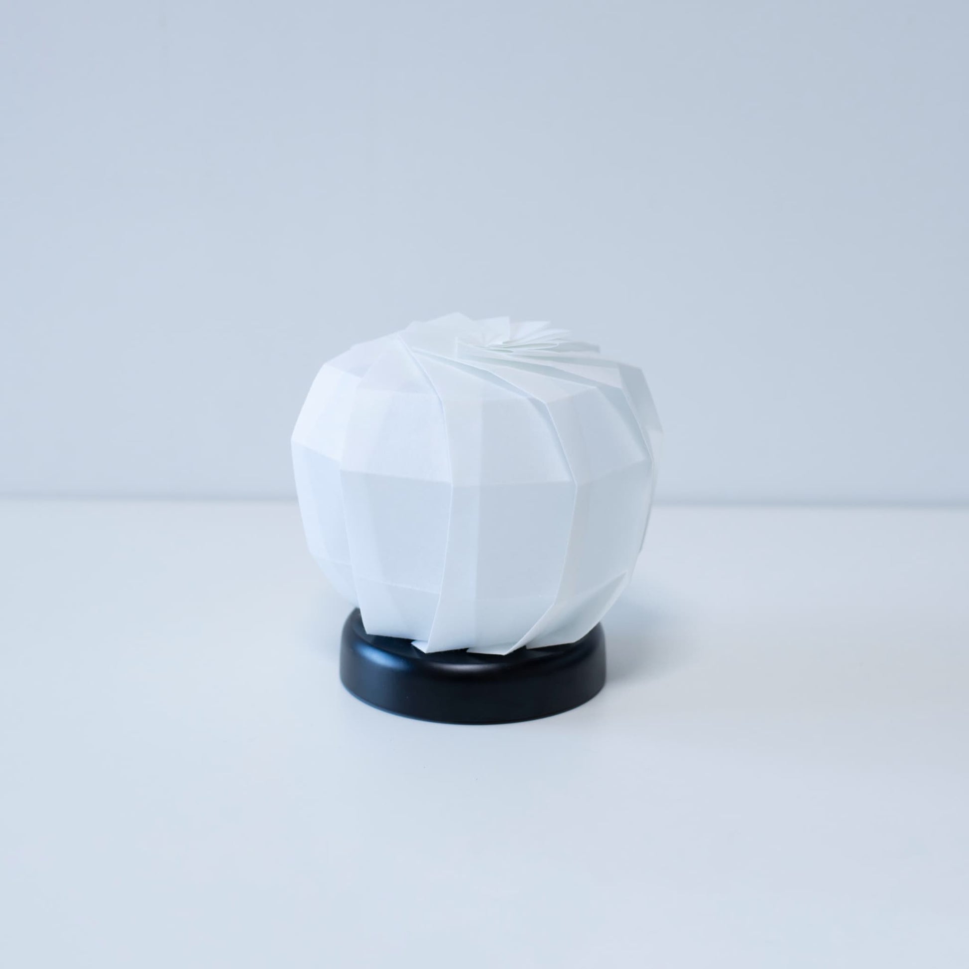 Modern Origami table lamp "maru M" with a black base and a white textured lampshade, creating a warm and inviting atmosphere in any room.