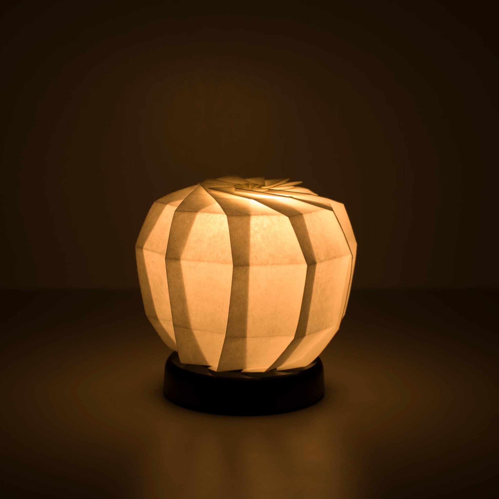 Origami Table lamp "maru M" with a black base and a spherical white lampshade crafted from intricately folded washi paper,  emitting a warm and inviting light.
