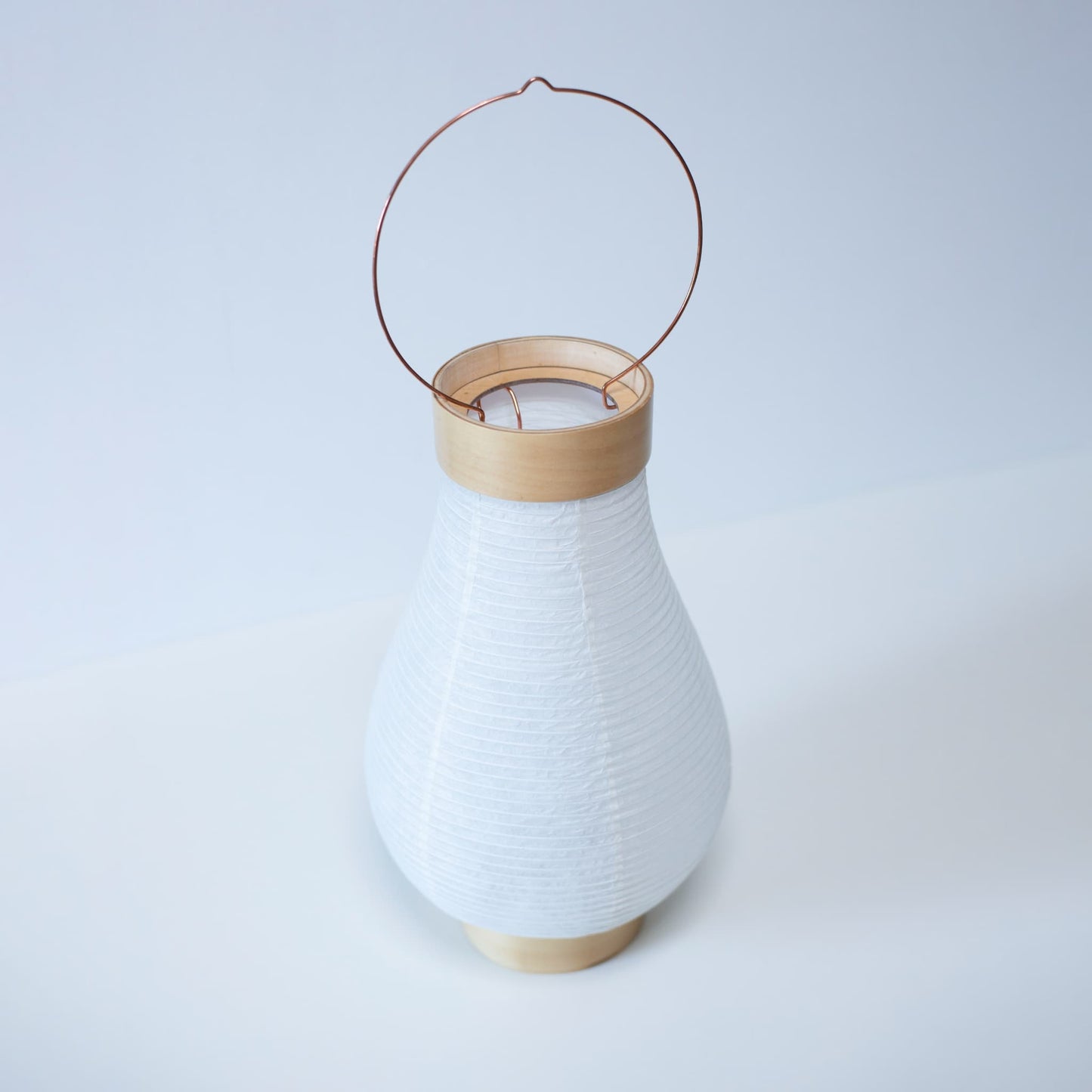 A traditional Japanese paper lantern photographed from above against bright white wallpaper